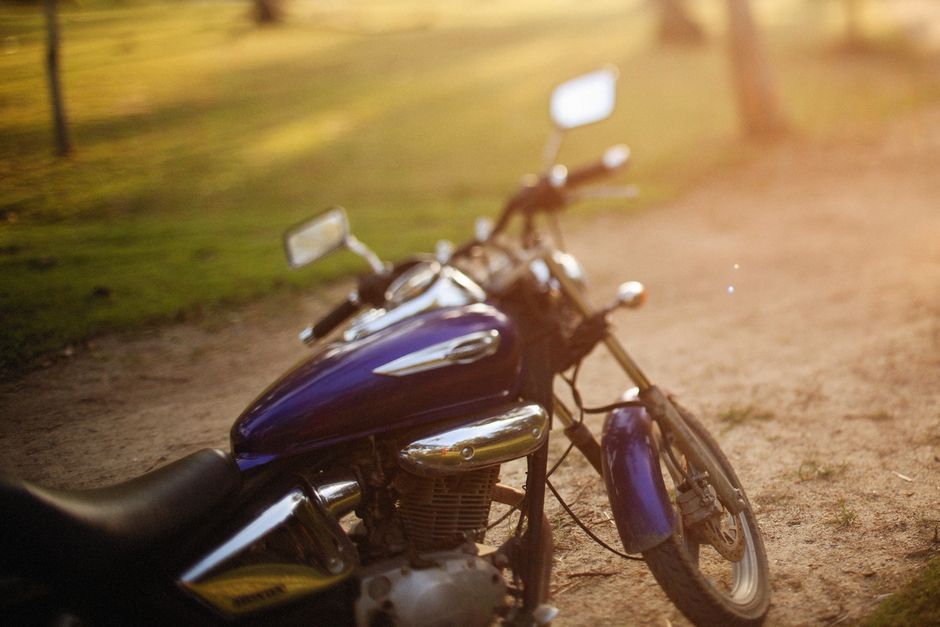 Close-up of a polished motorcycle parked on a sunlit dirt road with green field background.