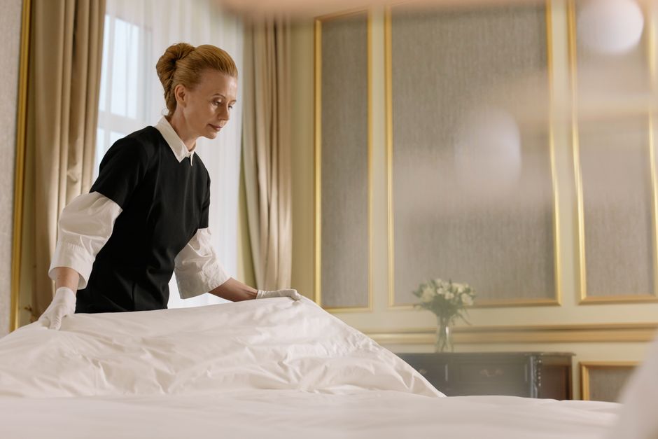 A professional housekeeper fixes a bed in a luxurious hotel room.