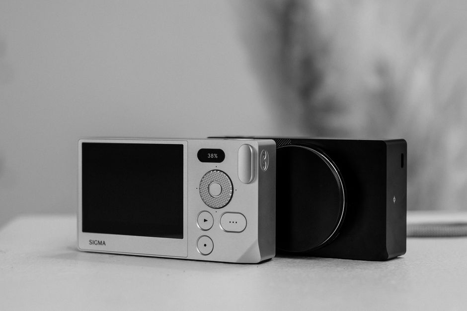 Monochrome close-up of a Sigma camera on a white surface, highlighting sleek design.