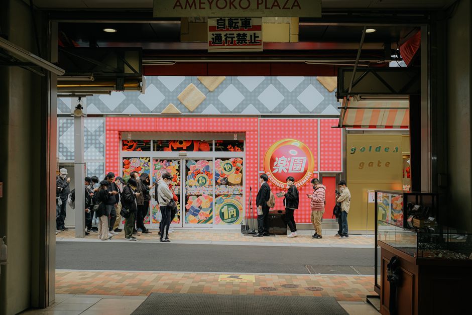 People lining up outside a colorful store in an Asian city, captured from a busy street setting.