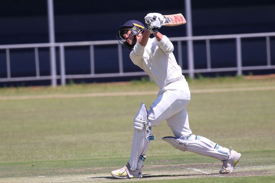 Cricketer in action hitting a shot on an outdoor field during a sunny day.