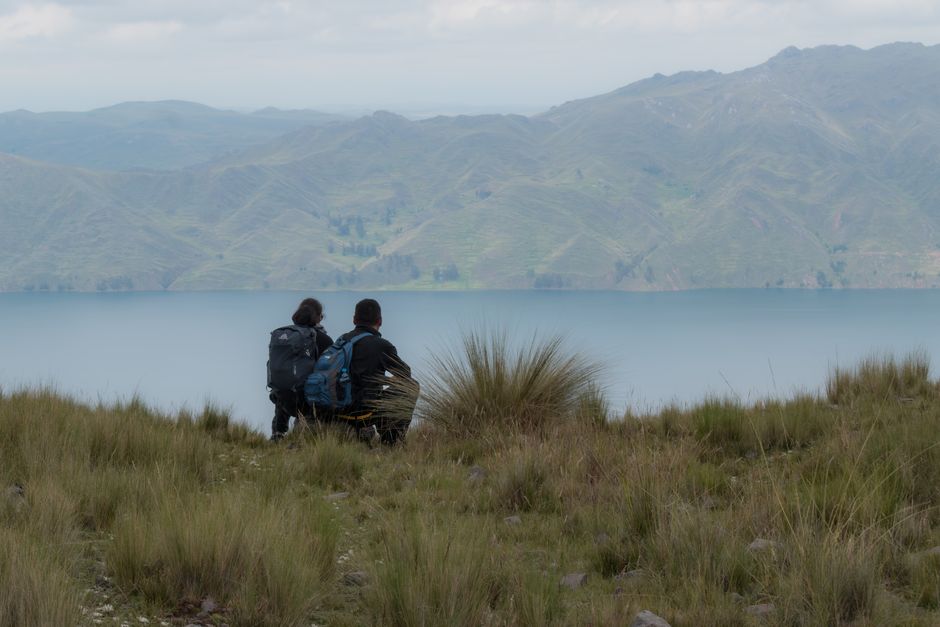 Two hikers enjoy a serene view over a lake and mountains in Cusco, Peru.