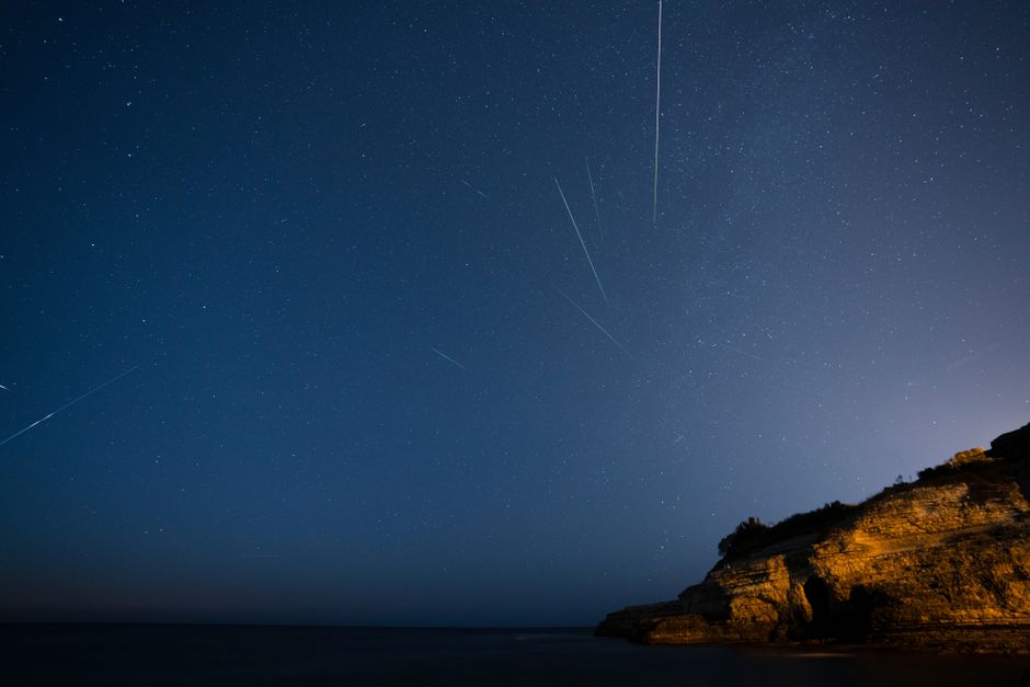 Beautiful starry sky with meteors streaking over a rocky cliff at night.