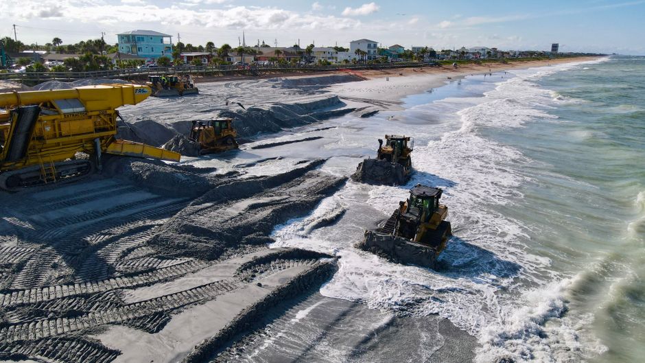 Heavy machinery operating on a beach for a coastal restoration project during daytime.