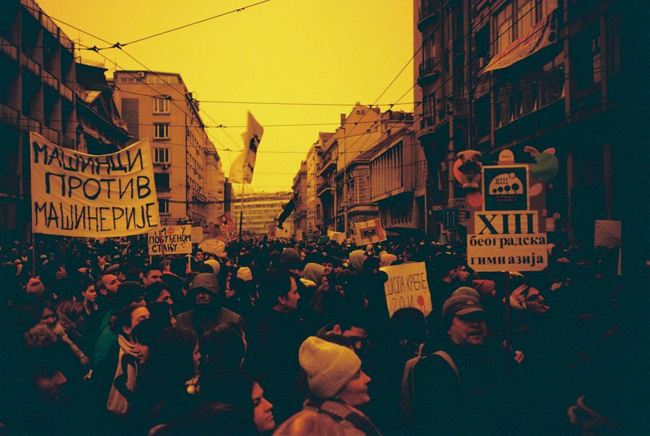 Large crowd demonstrating with banners in urban city street, vibrant atmosphere.