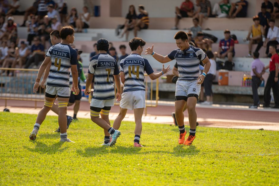 Teen rugby players celebrating a victory on a sunny day with enthusiastic teamwork.